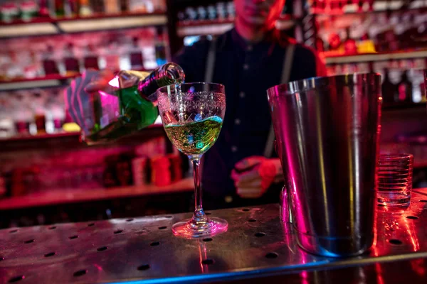 Barman termina a preparação de coquetel alcoólico, derramando bebida em luz de néon multicolorida, foco em vidro — Fotografia de Stock