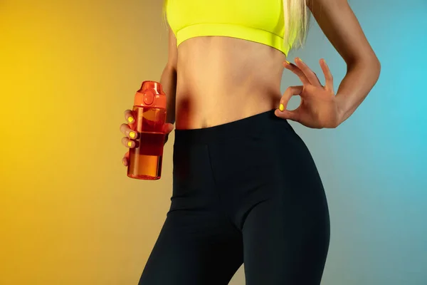 Close up of young and sportive woman with fit belly and well-kept skin holding red water bottle on gradient background. Perfect body ready for summertime. — Stock Photo, Image