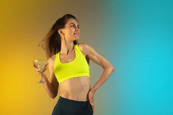 Fashion portrait of young fit and sportive woman drinking cocktail on gradient background. Perfect body ready for summertime. — Stock Photo, Image