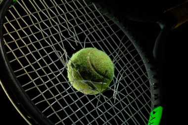 Siyah stüdyo arka planında izole edilmiş profesyonel spor ekipmanları. Tenis raketi ve top.