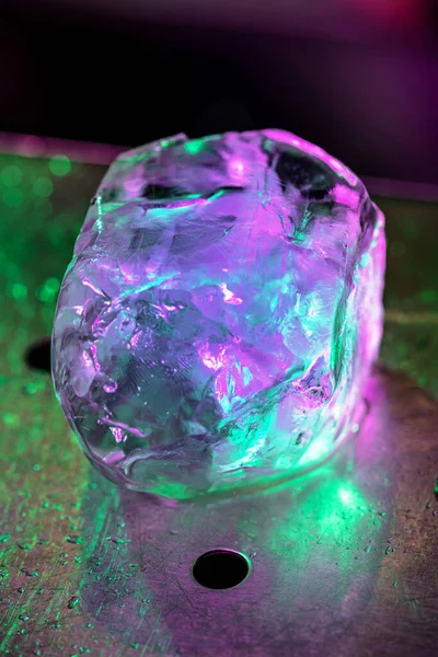 Gros plan gros morceau de glace fondante sur le comptoir du bar en néon rose-vert, préparation pour un cocktail — Photo