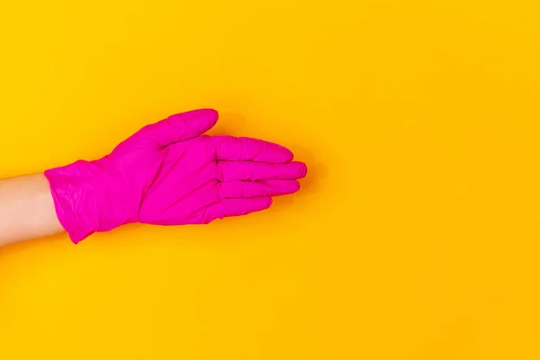 Χέρι σε ροζ γάντι καουτσούκ χαιρετισμό απομονώνονται σε κίτρινο φόντο στούντιο με copyspace. — Φωτογραφία Αρχείου