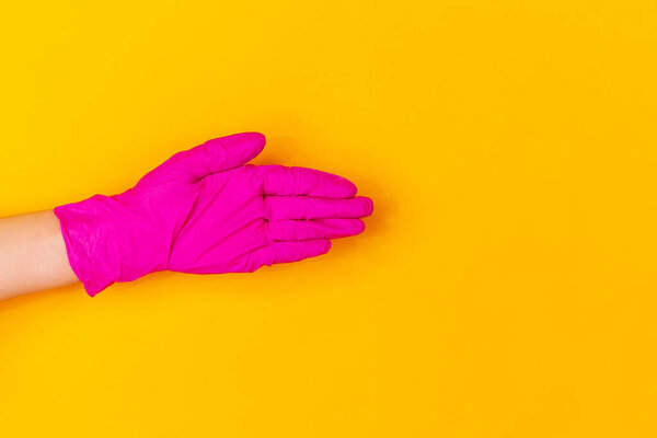 Hand in pink rubber glove greeting isolated on yellow studio background with copyspace.