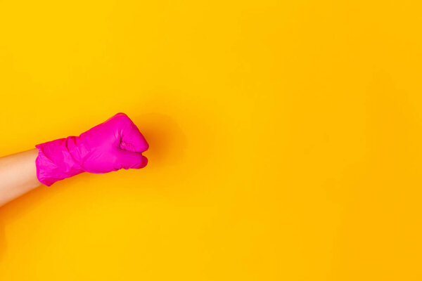 Hand in pink rubber glove showing fist bump isolated on yellow studio background with copyspace.