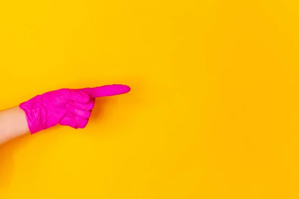 Mão na luva de borracha rosa apontando isolado no fundo do estúdio amarelo com copyspace . — Fotografia de Stock