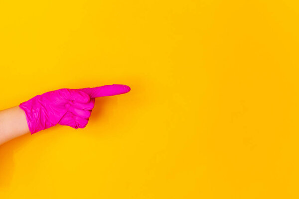 Hand in pink rubber glove pointing isolated on yellow studio background with copyspace.