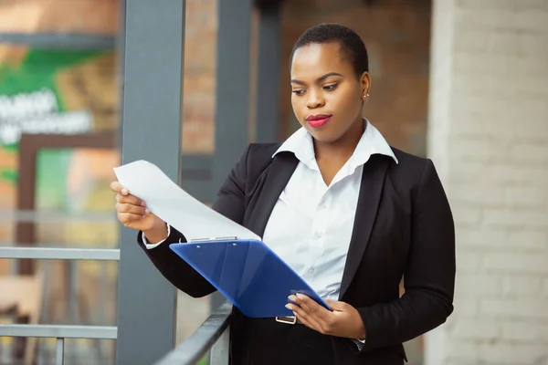 Mujer de negocios afroamericana en traje de oficina sonriendo, se ve confiada y feliz, exitosa —  Fotos de Stock