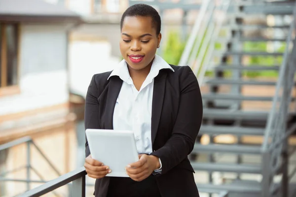 Mujer de negocios afroamericana en traje de oficina sonriendo, se ve confiada y feliz, exitosa —  Fotos de Stock