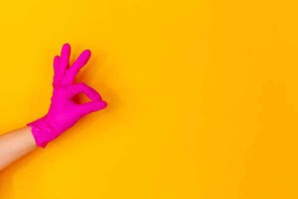 Mão na luva de borracha rosa mostrando bom sinal isolado no fundo do estúdio amarelo com copyspace . — Fotografia de Stock