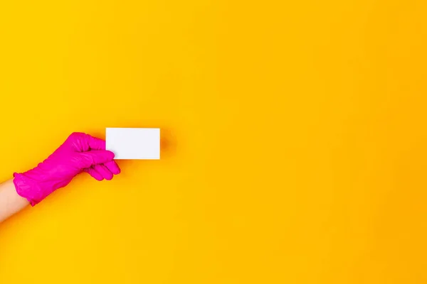Mão na luva de borracha rosa segurando cartão de visita isolado no fundo do estúdio amarelo com copyspace . — Fotografia de Stock