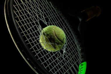 Siyah stüdyo arka planında izole edilmiş profesyonel spor ekipmanları. Tenis raketi ve top.