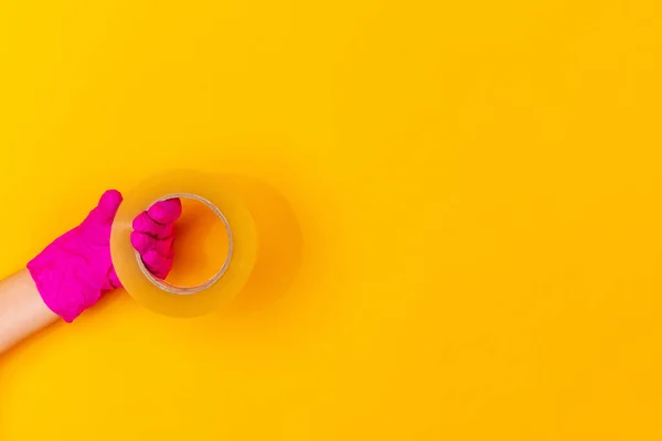 Mão na luva de borracha rosa segurando fita adesiva isolada no fundo do estúdio amarelo com copyspace . — Fotografia de Stock