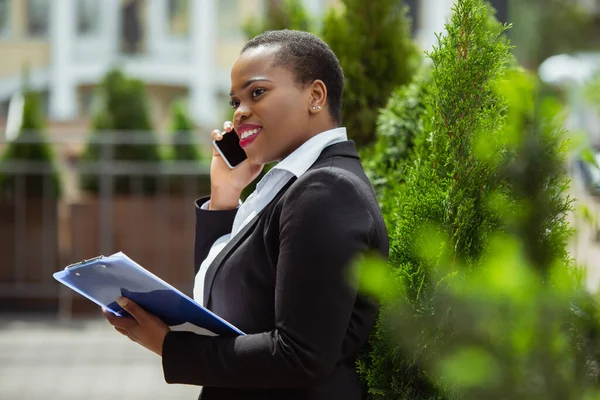 Mujer de negocios afroamericana en traje de oficina sonriendo, se ve confiada y feliz, exitosa —  Fotos de Stock