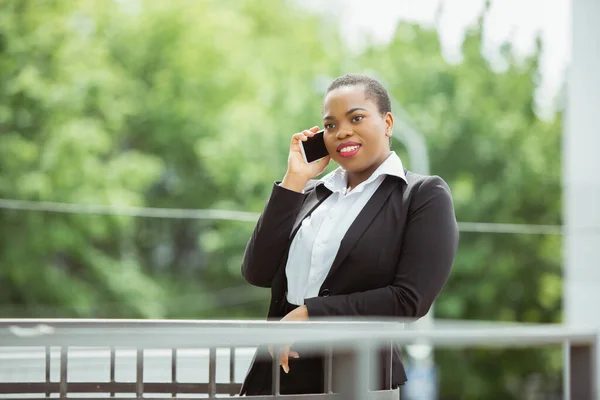 Mujer de negocios afroamericana en traje de oficina sonriendo, se ve confiada y feliz, exitosa —  Fotos de Stock