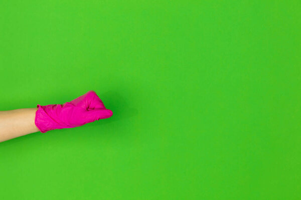 Hand in pink rubber glove shows fist bump isolated on green studio background with copyspace.