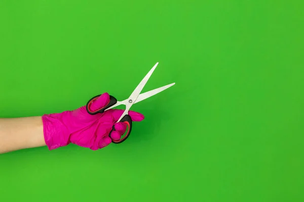 Рука в розовой резиновой перчатке держа ножницы изолированы на зеленом фоне студии с копирайтом . — стоковое фото