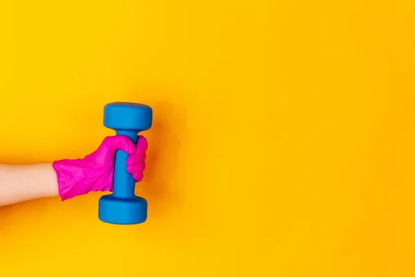 분홍색 고무 장갑을 손에 들고 덤벨을 들고, 노란색 스튜디오 배경에 복사 공간으로 격리 된 체육관 무게. — 스톡 사진