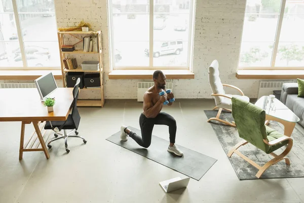 Hombre afroamericano joven entrenando en casa durante la cuarentena del brote de coronavirus, ejercicios de doinc de fitness, aeróbicos. Mantener el aislamiento deportivo asegurando . —  Fotos de Stock