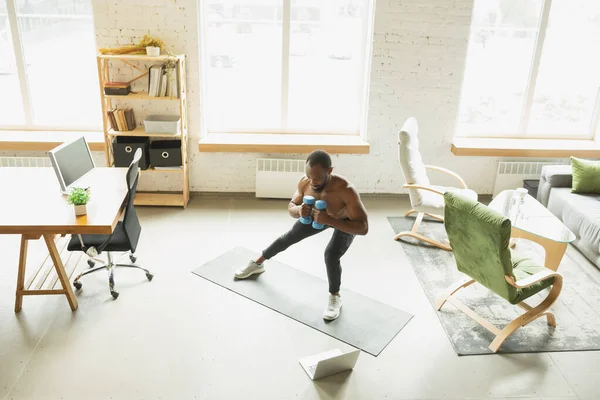 Młody Afrykańczyk-Amerykanin trenujący w domu podczas kwarantanny epidemii koronawirusu, doinc ćwiczenia fitness, aerobik. Utrzymanie sportowej izolacji zabezpieczającej. — Zdjęcie stockowe