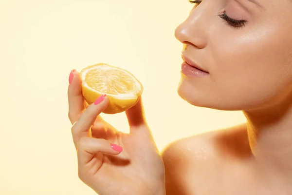Gros plan du beau visage féminin avec une tranche de citron sur fond jaune. Cosmétiques et maquillage, traitement naturel et écologique, soin de la peau . — Photo