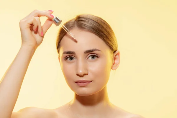 Bescherming. Close-up van mooie vrouwelijke gezicht met gieten etherische olie, serum over gele achtergrond. Cosmetica en make-up, natuurlijke en eco-behandeling, huidverzorging. — Stockfoto