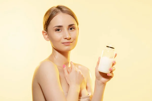 Glanzend. Close-up van mooie vrouw met moisturizer over gele achtergrond. Cosmetica en make-up, natuurlijke en eco-behandeling, huidverzorging. — Stockfoto