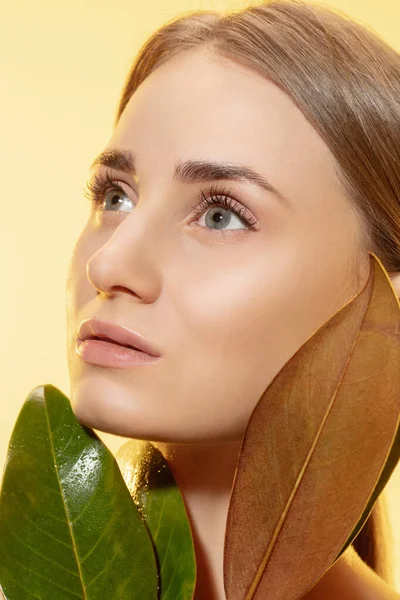 Nőies vagyok. Közelkép a gyönyörű női arc zöld levelek felett fehér háttér. Kozmetikumok és smink, természetes és ökoterápia, bőrápolás. — Stock Fotó