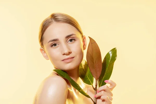 Femminile. Primo piano di bella faccia femminile con foglie verdi su sfondo bianco. Cosmetici e trucco, trattamento naturale ed ecologico, cura della pelle . — Foto Stock