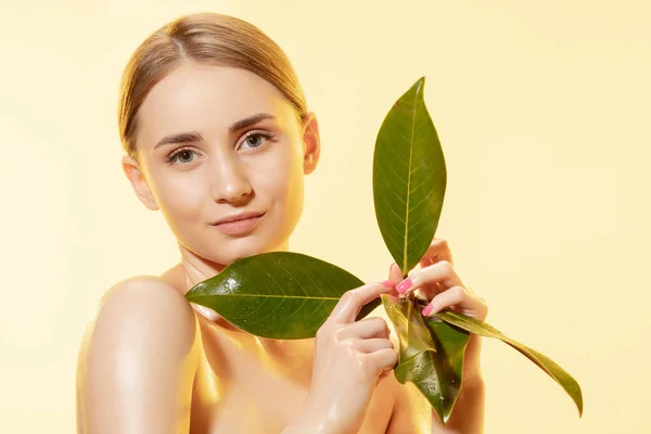 Vrouwelijk. Close-up van mooi vrouwelijk gezicht met groene bladeren over witte achtergrond. Cosmetica en make-up, natuurlijke en eco-behandeling, huidverzorging. — Stockfoto