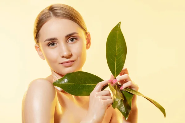 Feminino. Close up de belo rosto feminino com folhas verdes sobre fundo branco. Cosméticos e maquiagem, tratamento natural e ecológico, cuidados com a pele . — Fotografia de Stock