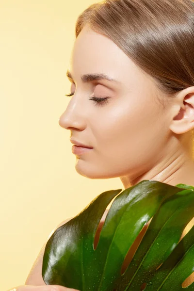 Glanzend. Close-up van mooi vrouwelijk gezicht met groene bladeren over witte achtergrond. Cosmetica en make-up, natuurlijke en eco-behandeling, huidverzorging. — Stockfoto