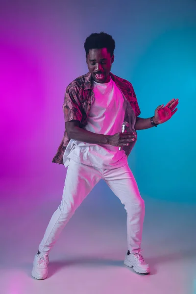 Retrato de cantor masculino afro-americano isolado no fundo do estúdio gradiente em luz de néon — Fotografia de Stock