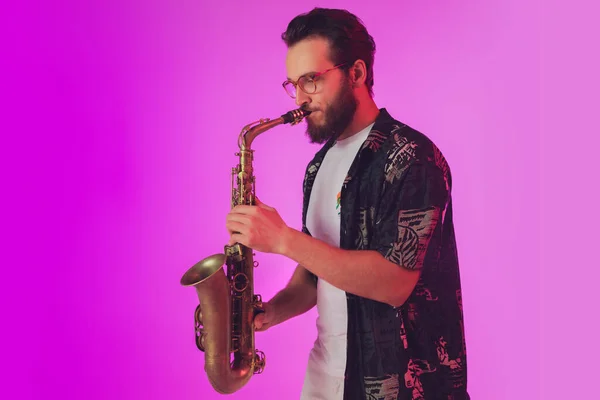 Jovem músico de jazz caucasiano tocando saxofone em luz de néon — Fotografia de Stock