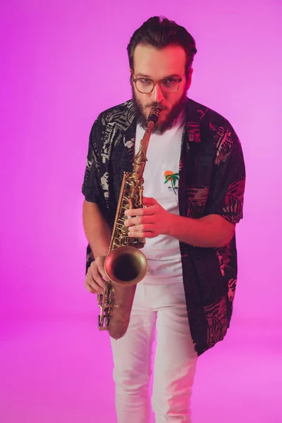 Jovem músico de jazz caucasiano tocando saxofone em luz de néon — Fotografia de Stock