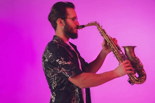 De jonge Kaukasische jazzmuzikant speelt de saxofoon in neonlicht — Stockfoto