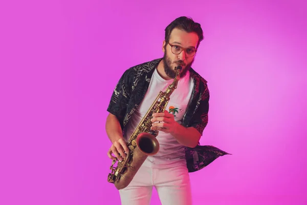 Jovem músico de jazz caucasiano tocando saxofone em luz de néon — Fotografia de Stock