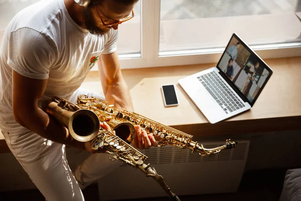 Músico caucásico tocando saxofón durante concierto en casa aislado y en cuarentena, improvisación impresionante con banda conectada en línea — Foto de Stock