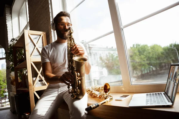 Músico caucasiano tocando saxofone durante concerto em casa isolado e em quarentena, improvisando impressionante com banda conectada online — Fotografia de Stock