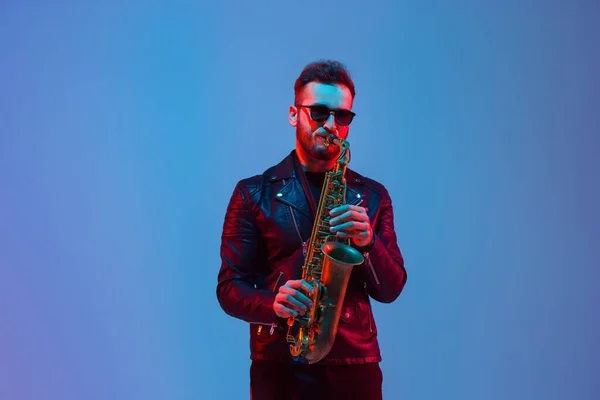 Jovem músico de jazz caucasiano tocando saxofone em luz de néon — Fotografia de Stock