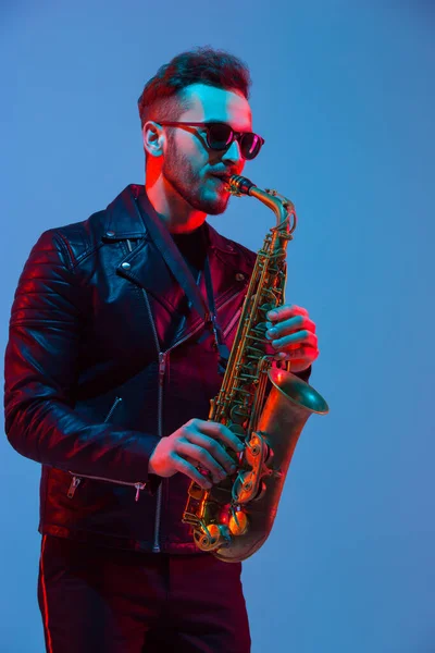 Mladý kavkazský jazzový hudebník hrající na saxofon v neonovém světle — Stock fotografie