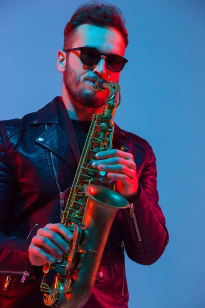 Joven músico de jazz caucásico tocando el saxofón con luz de neón — Foto de Stock