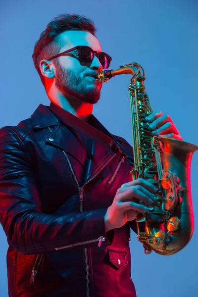 Young caucasian jazz musician playing the saxophone in neon light
