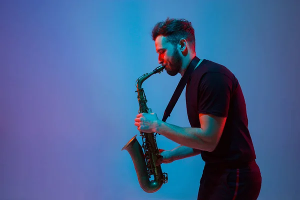 Young caucasian jazz musician playing the saxophone in neon light — Stock Photo, Image