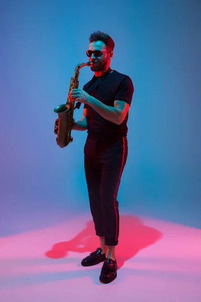 Joven músico de jazz caucásico tocando el saxofón con luz de neón — Foto de Stock