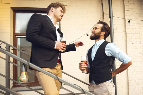Two men talking, celebrating, look happy, have corporate party at office or bar