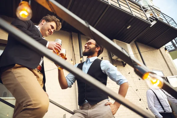 Two men talking, celebrating, look happy, have corporate party at office or bar