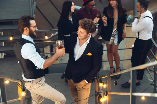 Corporativo celebrando en la cálida luz de las lámparas en la noche de verano, los jóvenes amigos, colegas se ven felices, hablan, se divierten — Foto de Stock