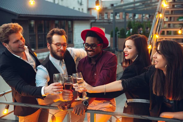 Corporativo celebrando en la cálida luz de las lámparas en la noche de verano, los jóvenes amigos, colegas se ven felices, hablan, se divierten, aplausos — Foto de Stock