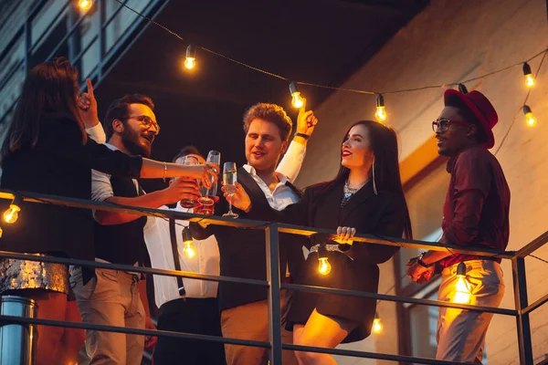 Corporativo celebrando en la cálida luz de las lámparas en la noche de verano, los jóvenes amigos, colegas se ven felices, hablan, se divierten, aplausos — Foto de Stock