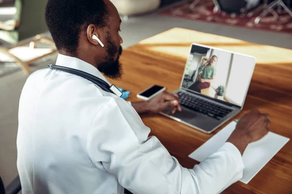 Arts adviseert de patiënt online met laptop. Afro-Amerikaanse arts tijdens zijn videocall, werken met patiënten, het uitleggen van recepten voor drugs. — Stockfoto